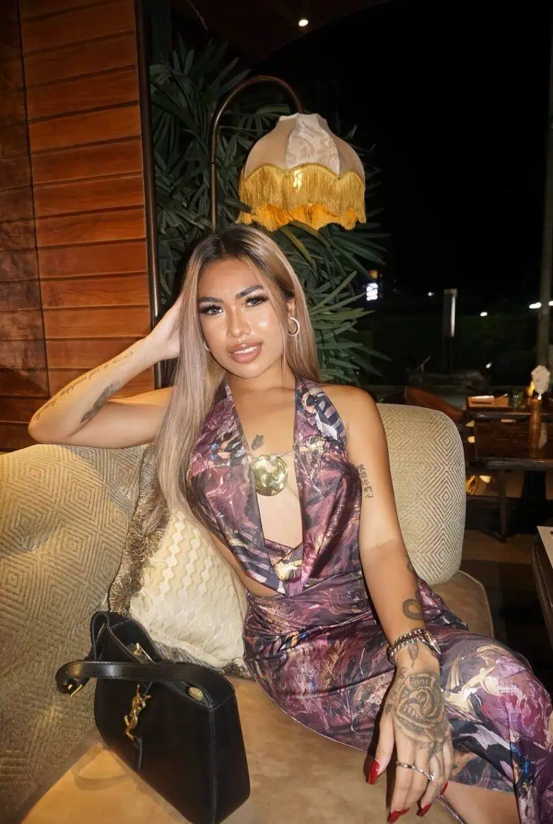 London escort, glamorous woman in trendy outfit sitting on sofa at night.