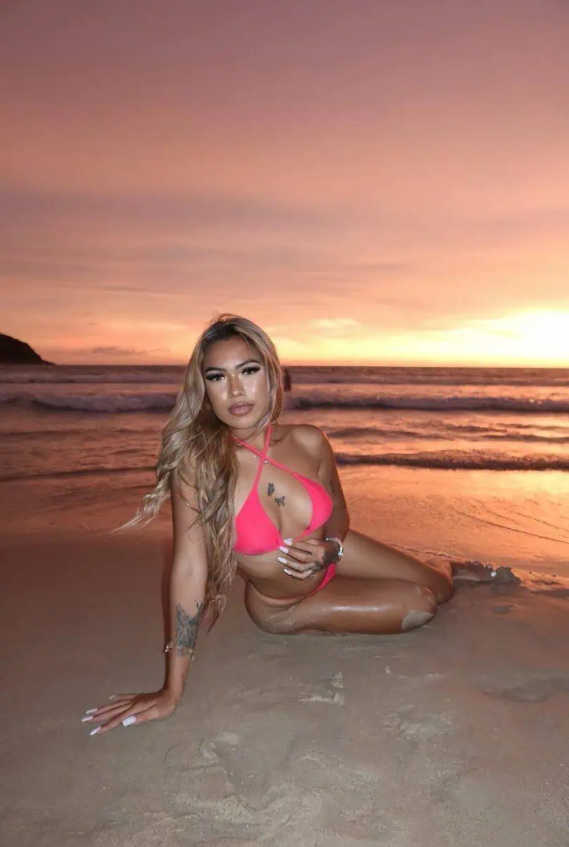 Glamorous woman in pink swimsuit on beach at sunset, Dubai Escorts, London escorts, intimate adult services, premium escort agency.