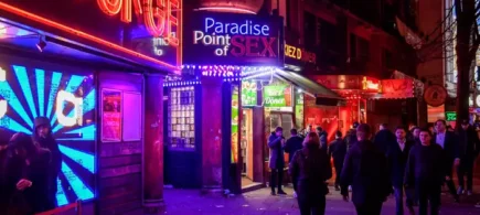 Neon-lit night scene outside lounge and adult entertainment venue in London, provocative nightlife atmosphere.
